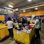 Cradles to Crayons   Volunteers sort donated clothing on yellow bins in a warehouse donation center with signs for clothing and sizing visible
